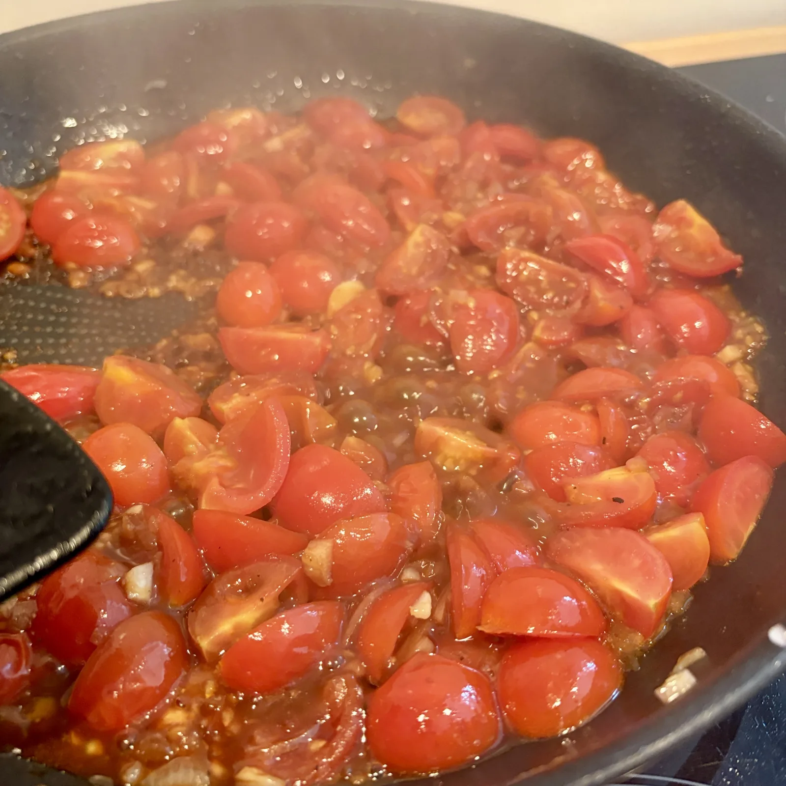 In einer großen Pfanne werden halbierte Kirschtomaten mit Knoblauch und Olivenöl angebraten. Die Tomaten sind bereits weich und saftig und bilden eine aromatische Tomatensauce.
