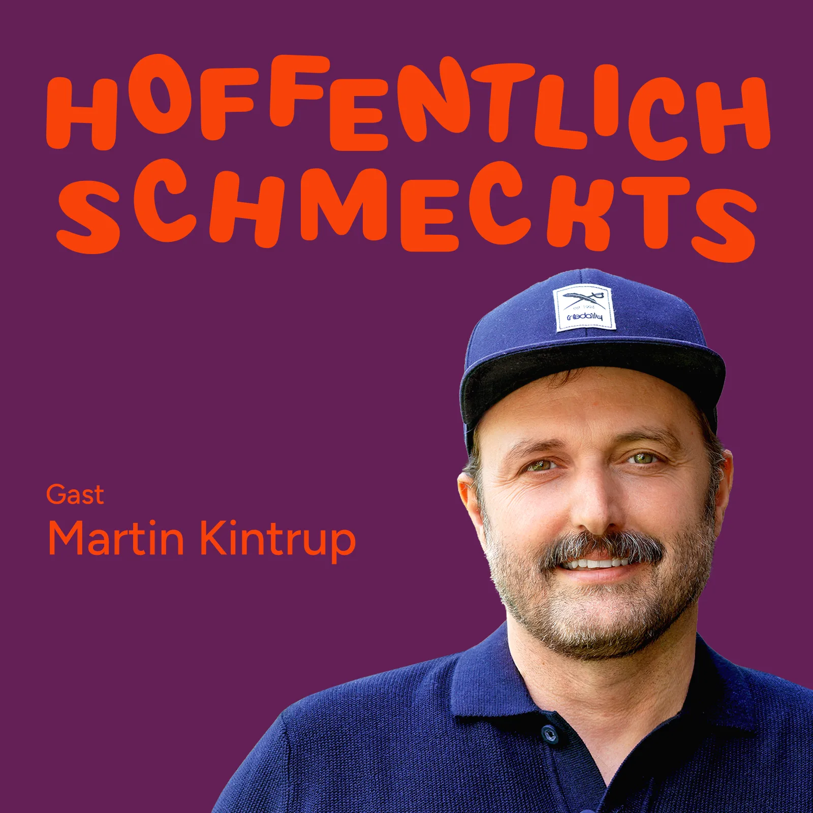 Porträt von Martin Kintrup mit dunkelblauer Cap und Strickpolo, lächelnd an eine alte Holztür gelehnt.