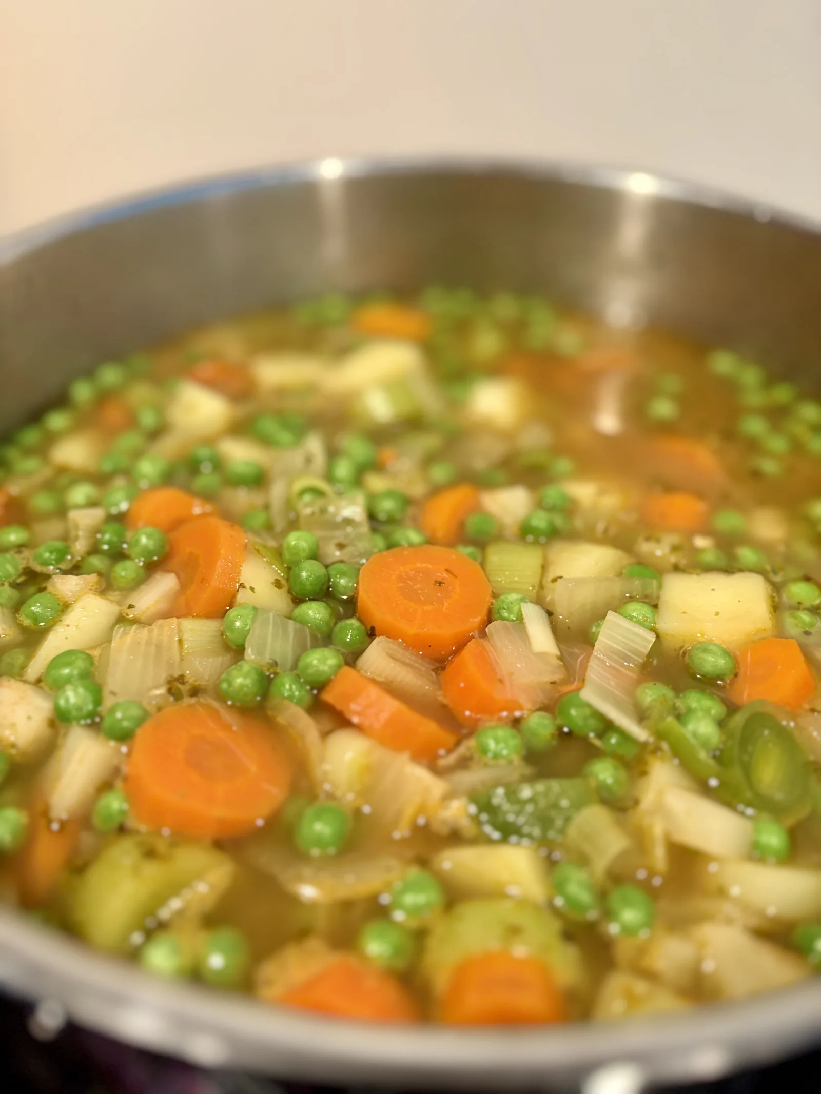Nahaufnahme von Omas Gemüsesuppe mit Erbsen, Karotten, Kartoffeln und Lauch in einer hellen Schüssel. Das bunte Gemüse liegt in einer würzigen, goldgelben Brühe und macht die Suppe besonders appetitlich.
