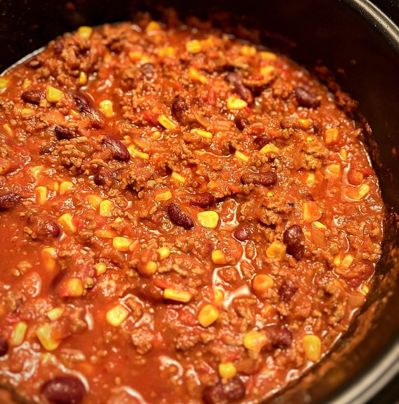 Chili con Carne mit Rinderhack, Kidneybohnen und Mais in würziger Tomatensoße im schwarzen Topf